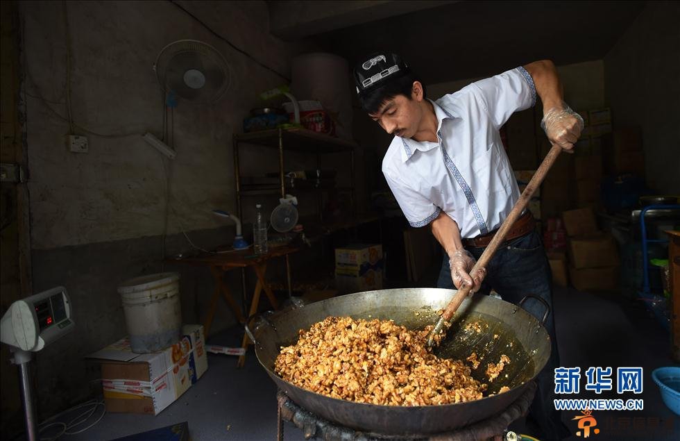 5月22日，阿迪力和蒋春杨一起将核桃仁倒入盛有糖稀的锅中。 新华社记者 李尕 摄